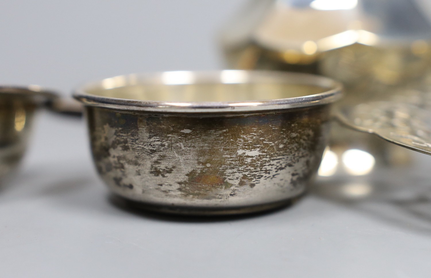 A George V engine turned silver mounted cigarette box, a similar sugar caster and later silver tea strainer and small dish.